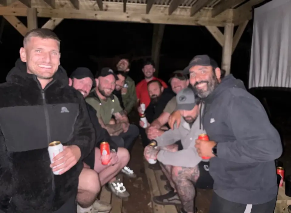 Attendees under the camp shelter at night, lit by lamps and the fire.