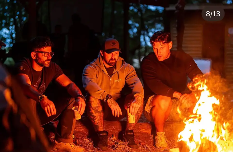 Attendees seated in a circle around the burning fire pit after dark.